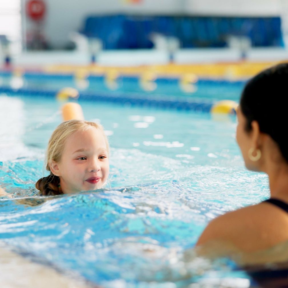 Mädchen lernt mit Schwimmnudel im Schwimmbecken schwimmen