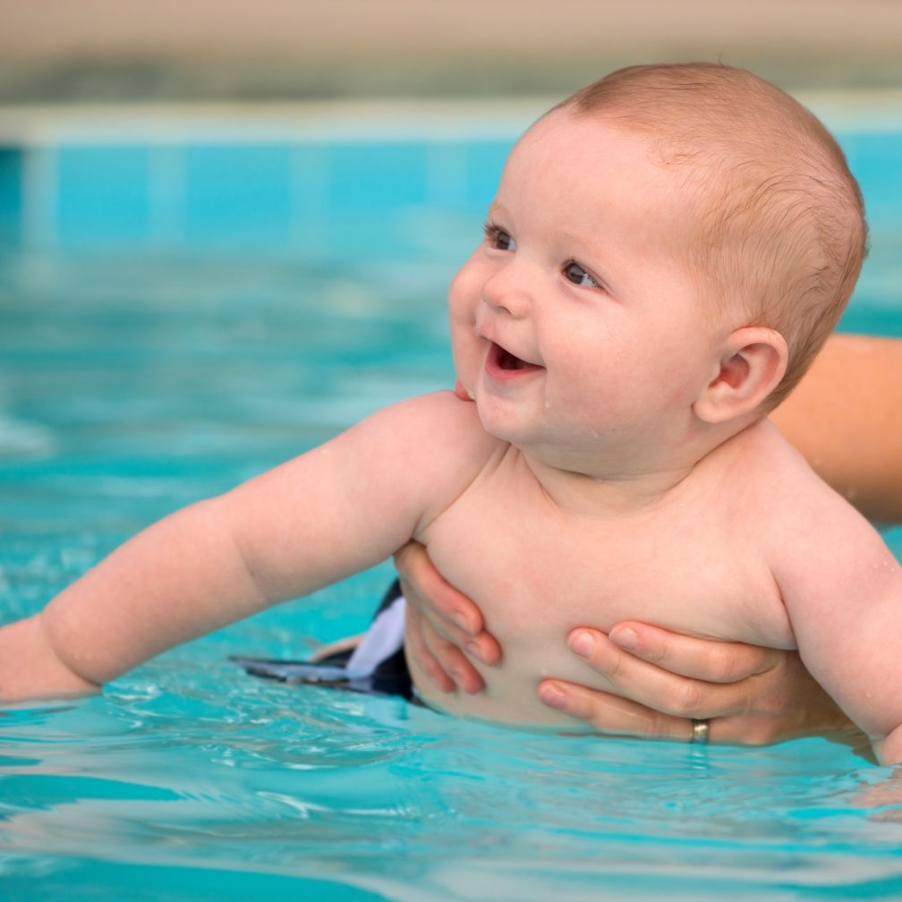 Baby im Schwimmbecken wird von einem Elternteil gehalten